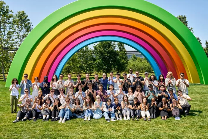 Foto grup pemenang Swift Student Challenge berpose di bawah instalasi pelangi besar Apple Park, merayakan kesuksesan.