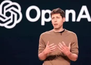 CEO OpenAI, Sam Altman, berbicara di atas panggung dengan logo OpenAI di latar belakang.