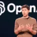CEO OpenAI, Sam Altman, berbicara di atas panggung dengan logo OpenAI di latar belakang.