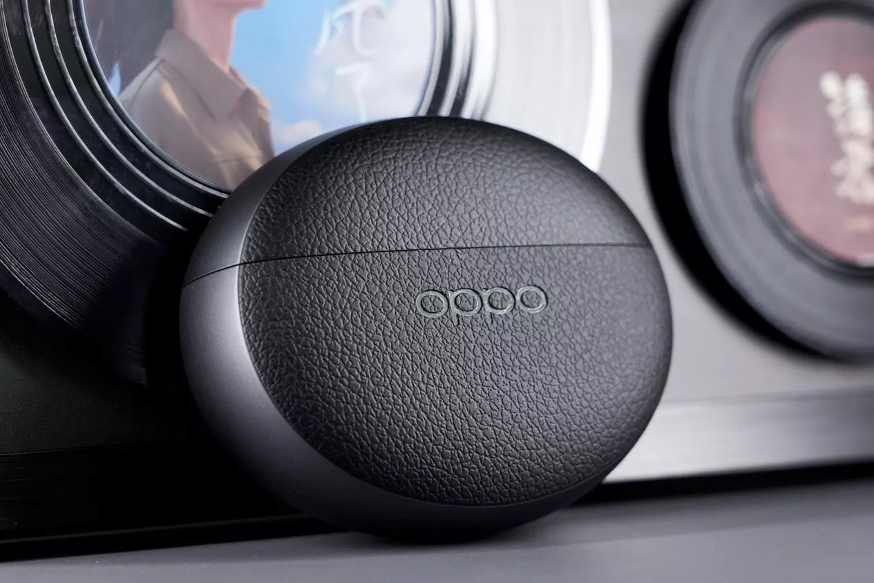 Casing earbuds TWS Oppo Enco berwarna hitam dengan tekstur kulit, menampilkan logo Oppo di bagian tengah casing bundar.