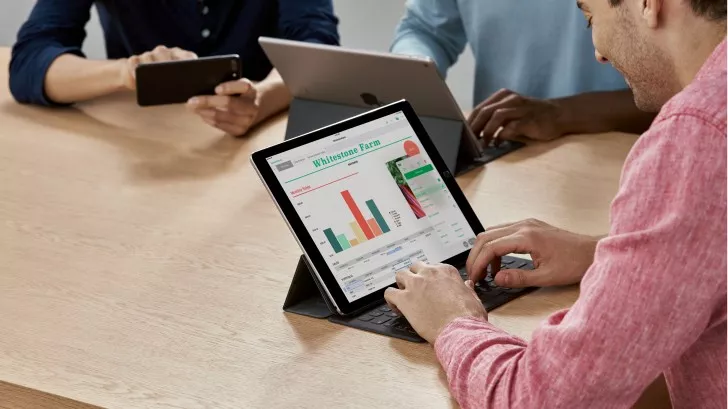 Seseorang mengetik di keyboard tablet yang menampilkan grafik data dan spreadsheet di layar, dalam suasana rapat.