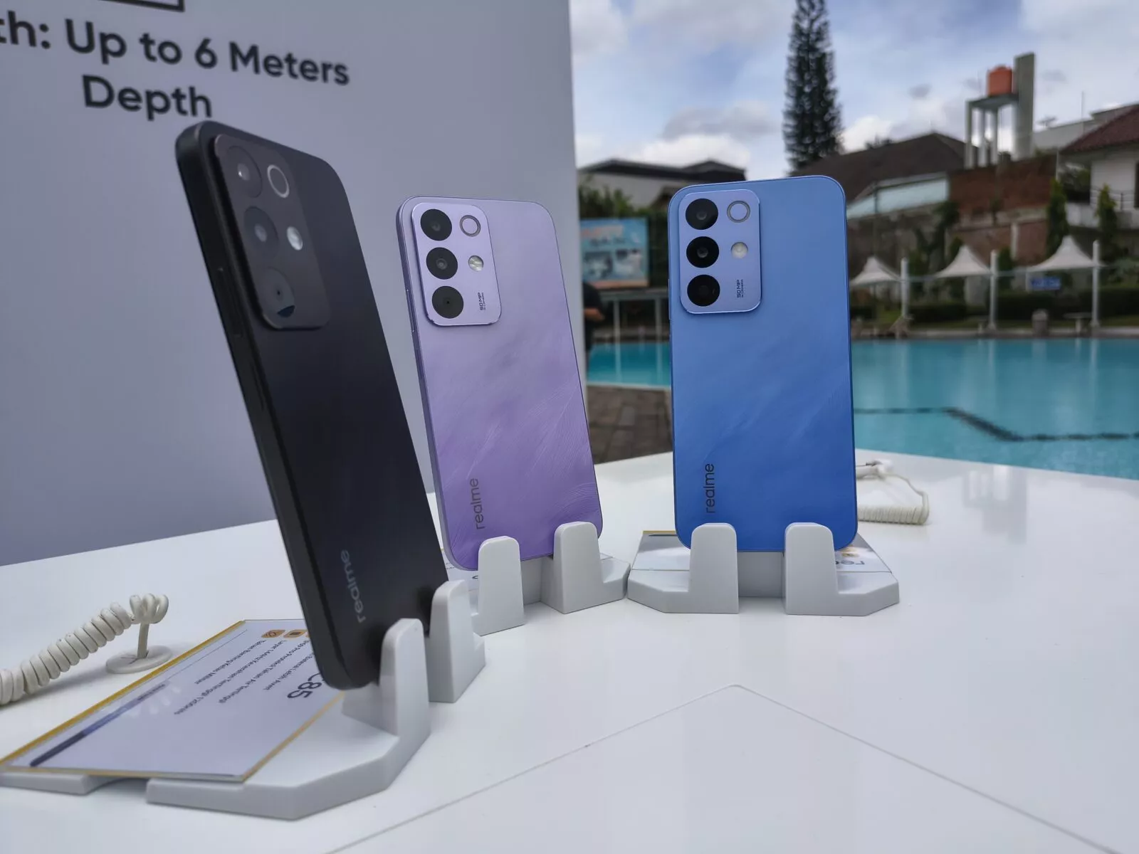 Tampilan close-up ponsel Realme C85 yang terlihat basah/terkena percikan air, menunjukkan desain tahan air.