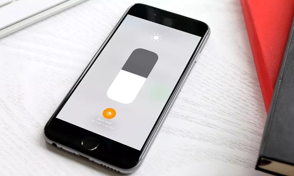 Layar iPhone menampilkan slider kecerahan di Control Center, dengan ikon Night Shift aktif di bagian bawah.