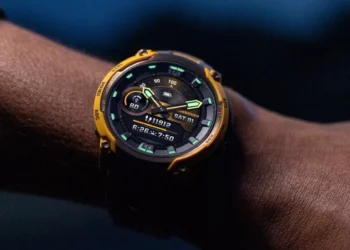Close-up jam tangan Garmin Instinct Crossover AMOLED berwarna kuning di pergelangan tangan, menunjukkan tampilan hybrid digital dan analog.