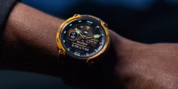 Close-up jam tangan Garmin Instinct Crossover AMOLED berwarna kuning di pergelangan tangan, menunjukkan tampilan hybrid digital dan analog.