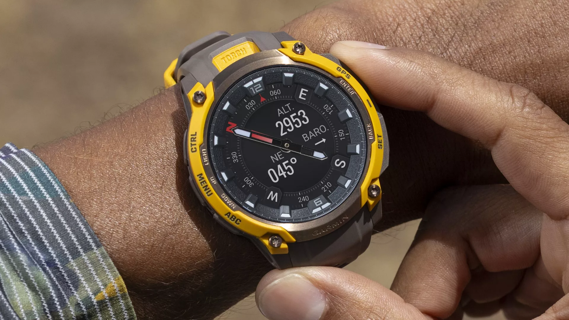 Close-up tangan memegang Garmin Instinct Crossover AMOLED, menampilkan data navigasi termasuk ketinggian (ALT 2953) dan kompas.