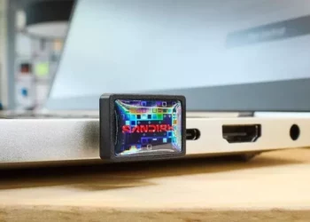 Flash drive SanDisk USB-C berukuran kecil terpasang pada port USB-C laptop berwarna putih, menampilkan logo SanDisk di permukaannya.