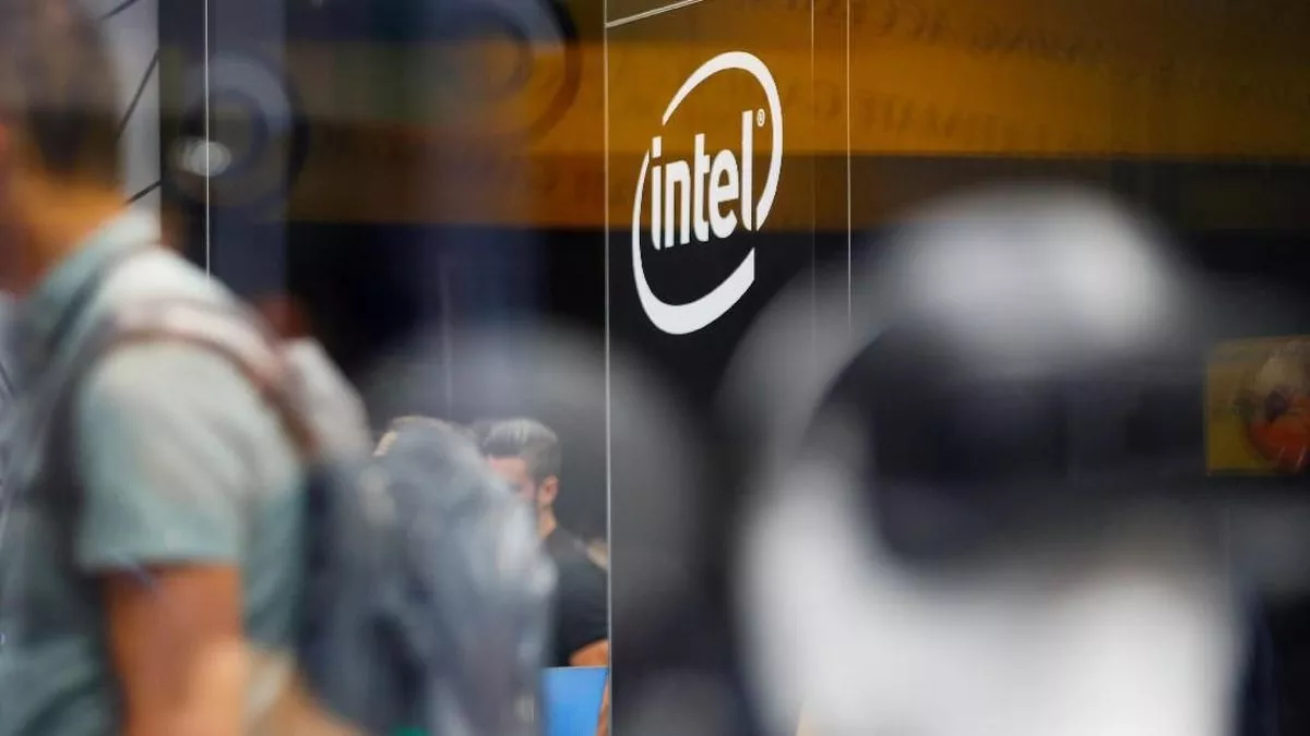 Logo Intel terlihat dari luar di jendela kaca sebuah gedung, dengan siluet orang yang bergerak di dalamnya.