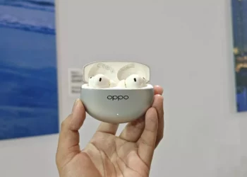 Satu set earbuds nirkabel TWS Oppo Enco berwarna putih di dalam casing pengisi daya berwarna perak, dipegang oleh tangan.