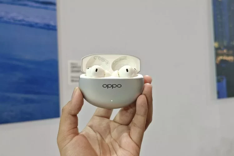 Satu set earbuds nirkabel TWS Oppo Enco berwarna putih di dalam casing pengisi daya berwarna perak, dipegang oleh tangan.