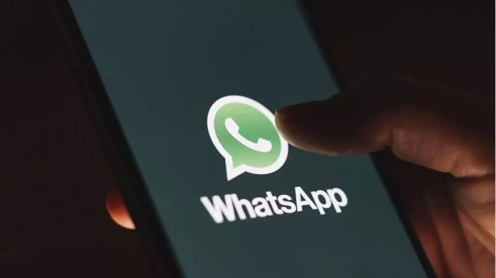 Logo WhatsApp di layar smartphone yang gelap, dengan jari sedang menyentuh layar.