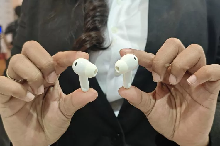Sepasang earbuds TWS Oppo Enco berwarna putih dipegang oleh dua tangan di depan setelan jas, menunjukkan desain yang elegan dan profesional.