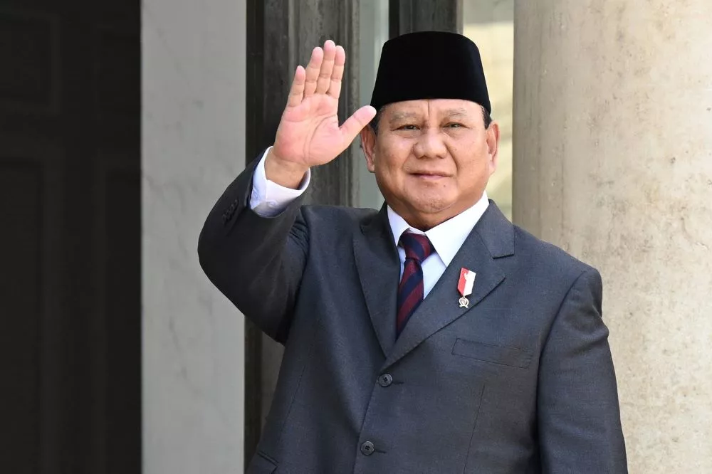 Presiden Prabowo Subianto mengenakan jas dan peci hitam, melambaikan tangan.