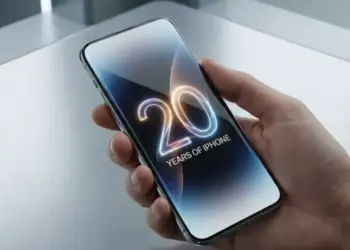 Tangan memegang smartphone iPhone Edisi 20 Tahun dengan layar bezel-less yang menampilkan angka "20" menyala neon, merayakan 20 tahun iPhone.