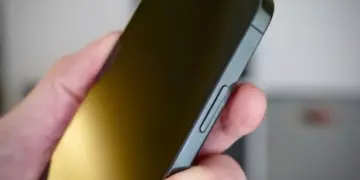 Jari pengguna menekan bagian tepi layar iPhone untuk mencoba cara menghidupkan HP tanpa tombol melalui aksesori atau koneksi kabel.