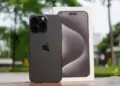 Unit iPhone 15 Pro berwarna hitam matte yang diletakkan di samping kotak kemasan aslinya dengan latar belakang luar ruangan yang fokus.