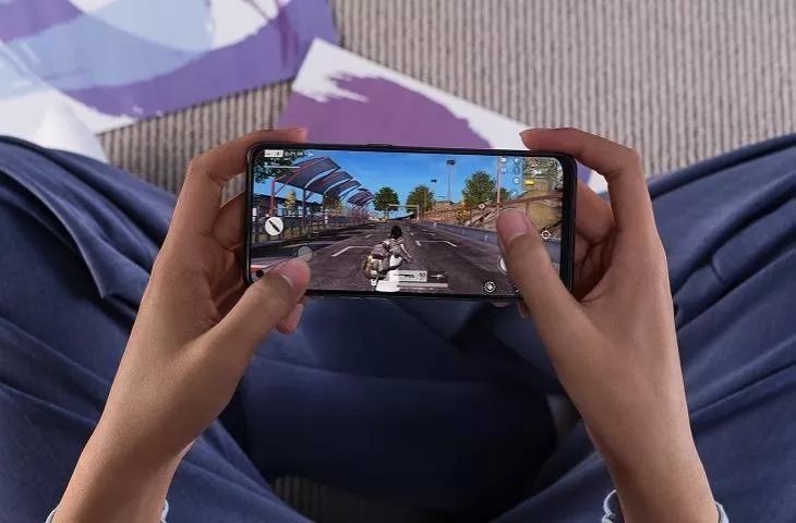 Seorang pria sedang fokus bermain game di ponsel secara horizontal dengan latar belakang yang agak buram.