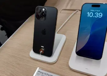 Dua unit iPhone 16 Pro Max dipajang di stand, satu menampilkan layar, dan satu menampakkan sisi belakang dan kamera.
