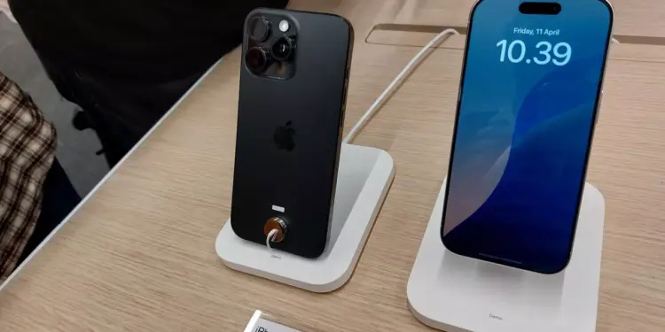 Dua unit iPhone 16 Pro Max dipajang di stand, satu menampilkan layar, dan satu menampakkan sisi belakang dan kamera.