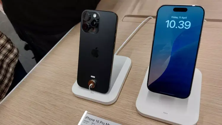 Dua unit iPhone 16 Pro Max dipajang di stand, satu menampilkan layar, dan satu menampakkan sisi belakang dan kamera.