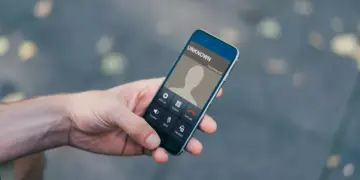 Close-up layar smartphone menunjukkan panggilan masuk dari "Unknown" dengan jari menekan tombol tolak (merah), mengisyaratkan bahaya.