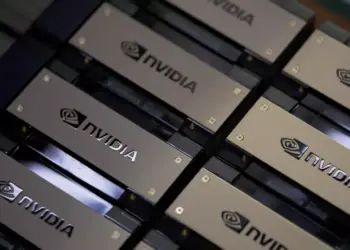 Tumpukan chip atau kartu grafis dengan logo NVIDIA berwarna emas di gudang pabrik, mengindikasikan peningkatan produksi Chip H200.