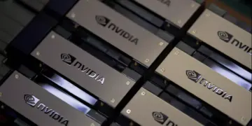 Tumpukan chip atau kartu grafis dengan logo NVIDIA berwarna emas di gudang pabrik, mengindikasikan peningkatan produksi Chip H200.