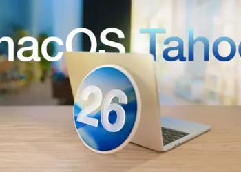 Logo macOS Tahoe dengan angka 26 di tengah diletakkan di depan laptop MacBook yang terbuka, menyoroti rilis update macOS Tahoe 26.2.