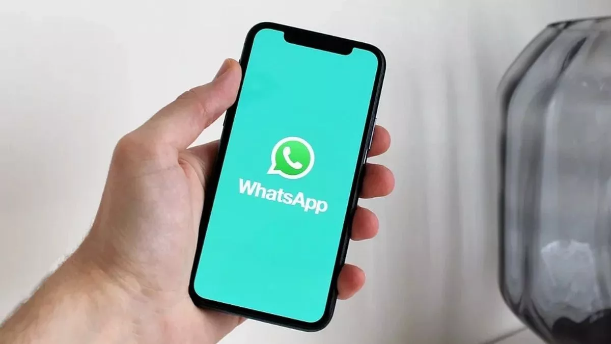 Seseorang memegang iPhone yang berhasil menampilkan logo WhatsApp setelah sukses memasukkan kode verifikasi WhatsApp.