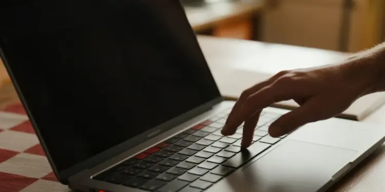 Tangan menekan keyboard laptop dengan layar hitam, memvisualisasikan masalah komputer mati total yang butuh perbaikan.