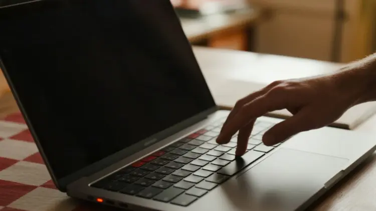 Tangan menekan keyboard laptop dengan layar hitam, memvisualisasikan masalah komputer mati total yang butuh perbaikan.