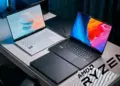 Setup studio menampilkan rekomendasi laptop AMD Ryzen terbaik 2025, termasuk Asus Zenbook putih dan Razer Blade hitam dengan logo AMD Ryzen.