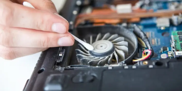 Tangan sedang membersihkan debu tebal pada bilah kipas laptop yang berisik, salah satu solusi utama untuk mengatasi masalah Kipas Komputer Berisik dan overheating.