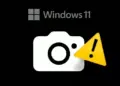 Ikon kamera dengan tanda seru kuning pada latar belakang Windows 11 untuk ilustrasi Tes Kamera di Windows 11 yang bermasalah.