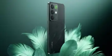 Realme C85 5G warna hijau gelap berdiri di atas dekorasi daun, menunjukkan sertifikasi militer dan bodi tangguh.