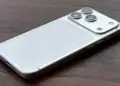 Detail bodi belakang iPhone 18 Pro Max warna putih perak di atas permukaan kayu, menonjolkan logo Apple dan lensa kamera.