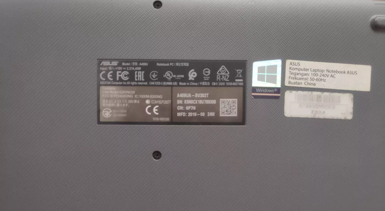 Stiker informasi pada bagian bawah laptop ASUS yang menunjukkan nomor model dan Serial Number Laptop.