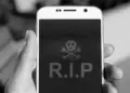 Layar smartphone menampilkan simbol tengkorak dan tulisan RIP sebagai ilustrasi HP mati total.