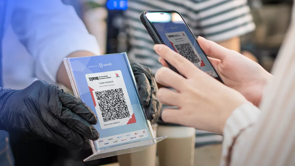 Proses transaksi QRIS antara pelanggan dan kasir yang menggunakan sarung tangan pelindung, menunjukkan pembayaran non-tunai yang higienis.