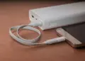 Sebuah smartphone sedang diisi daya menggunakan kabel putih yang terhubung ke Powerbank Terbaik 10.000 mAh di atas meja kayu.