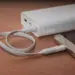 Sebuah smartphone sedang diisi daya menggunakan kabel putih yang terhubung ke Powerbank Terbaik 10.000 mAh di atas meja kayu.