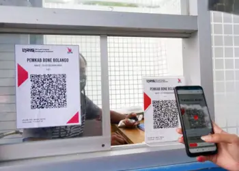 Penggunaan transaksi QRIS untuk pembayaran administrasi di loket pemerintah daerah melalui kaca pembatas.