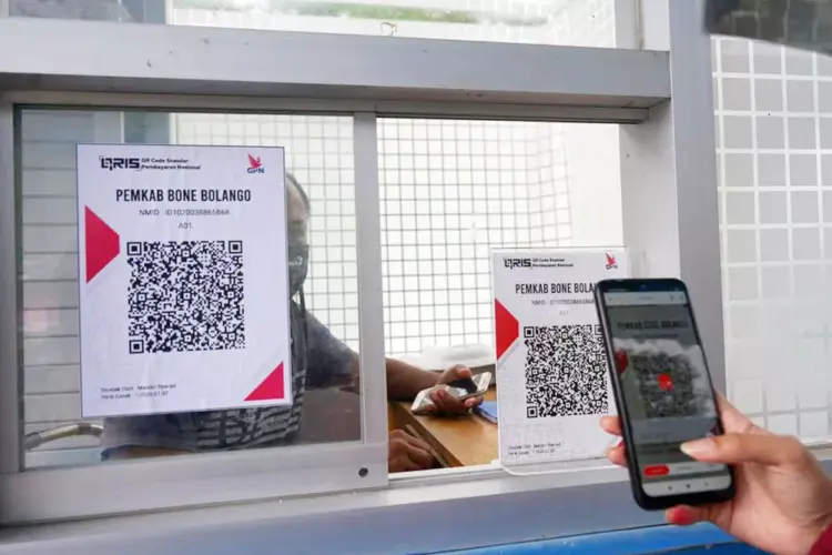 Penggunaan transaksi QRIS untuk pembayaran administrasi di loket pemerintah daerah melalui kaca pembatas.