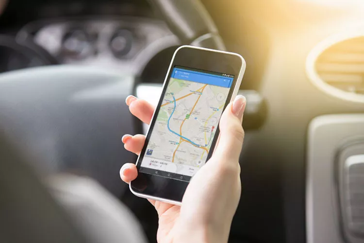 Tangan seseorang sedang memegang smartphone yang menampilkan peta digital dengan rute perjalanan mudik yang optimal.