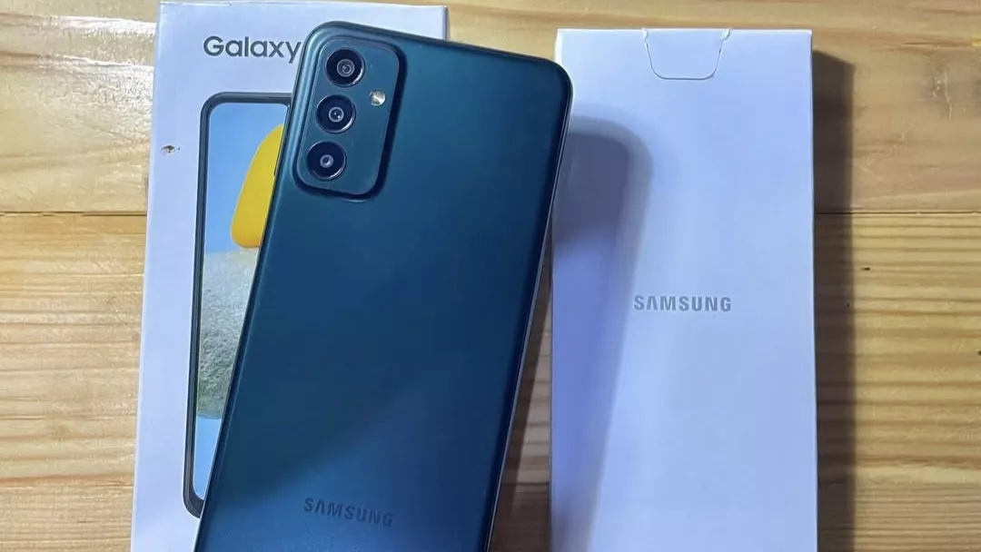 Desain bodi belakang dan modul kamera Samsung Galaxy M23 5G warna hijau gelap di atas meja kayu.
