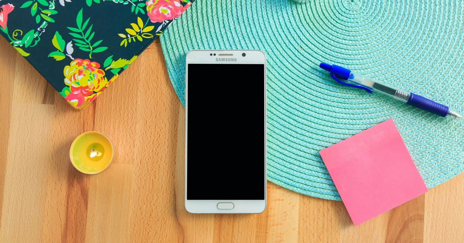 Smartphone Samsung putih di atas meja kayu dikelilingi alat tulis, menggambarkan perangkat yang memerlukan pengaturan screen timeout.