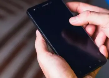 Tangan seseorang sedang mengoperasikan smartphone Android dengan layar gelap untuk mencoba mengubah setelan durasi layar.