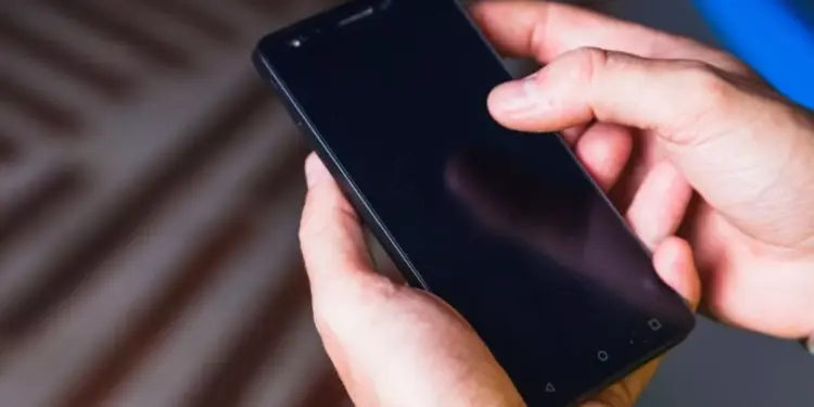 Tangan seseorang sedang mengoperasikan smartphone Android dengan layar gelap untuk mencoba mengubah setelan durasi layar.