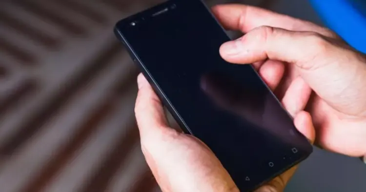 Tangan seseorang sedang mengoperasikan smartphone Android dengan layar gelap untuk mencoba mengubah setelan durasi layar.