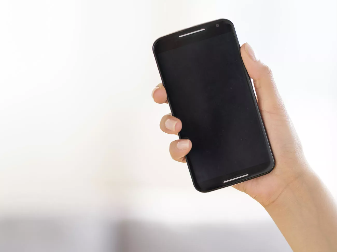 Tangan memegang smartphone dengan latar belakang terang, menunjukkan layar yang tetap stabil menyala setelah pengaturan durasi diubah.